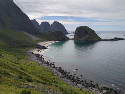 Cover image. A photo of Gjerdvika bay shot from a nearby hill. Sea on the right, lush green slopes on the left.