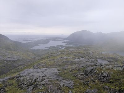 A photo portraying a ridge, with a faintly visible fjord in the background. The entire frame is covered by mist