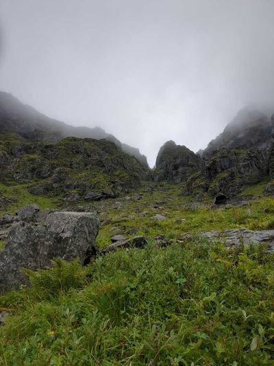 Photo of a narrow mountain pass. Top of the pass is obscured by clouds. Ground is covered in small boulders